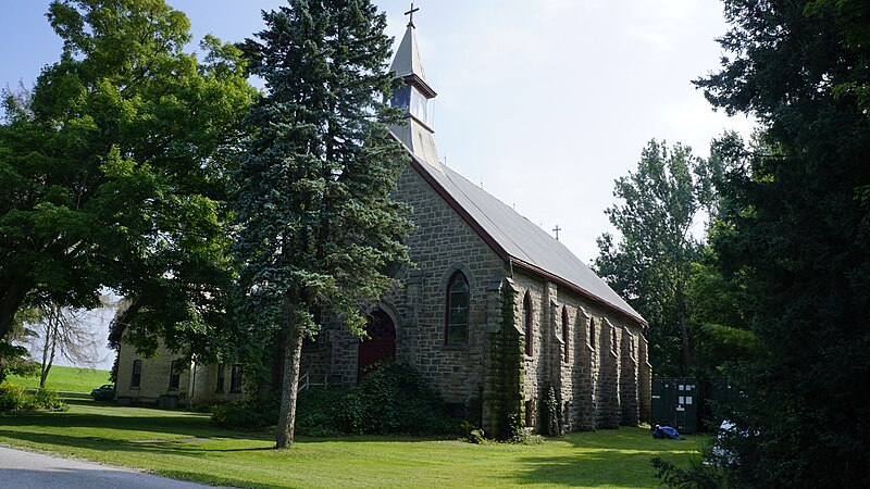 Stone Catholic church surrounded by trees and gras.